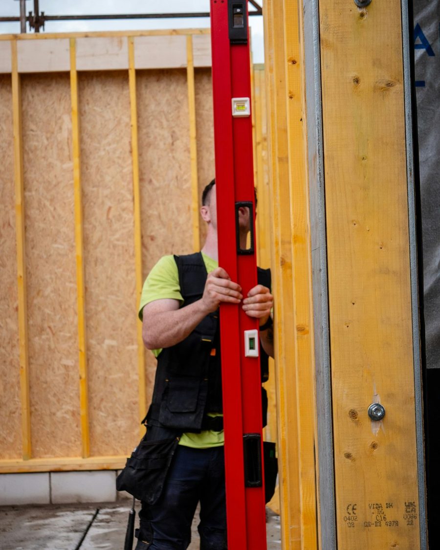 Menuisier vérifiant au niveau l'aplomb d'un mur à ossature bois en cours de montage